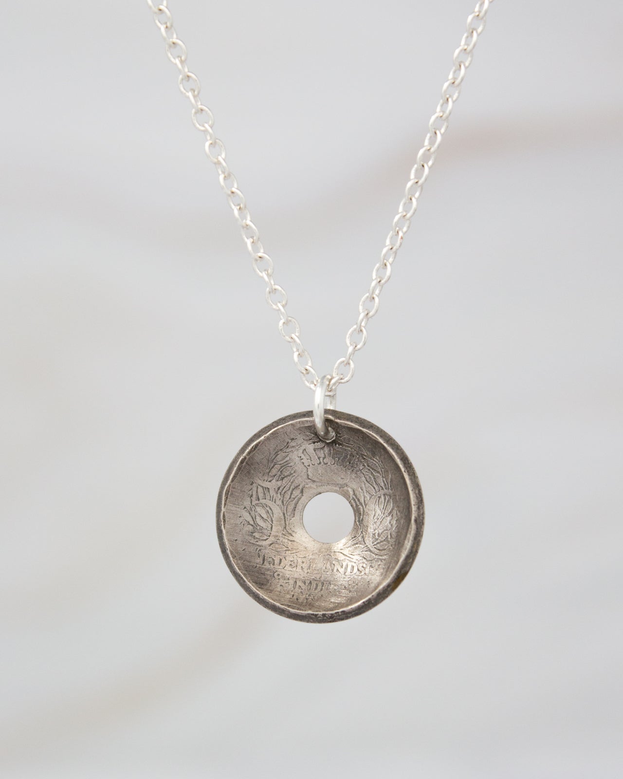 A silver necklace pendant with an engraved design on it.