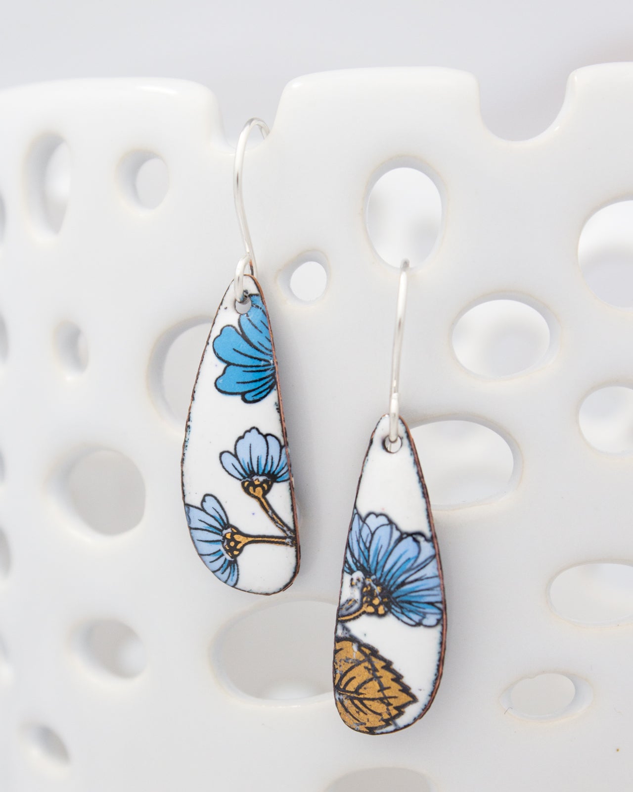 A pair of earrings with blue and white floral designs on a white surface.