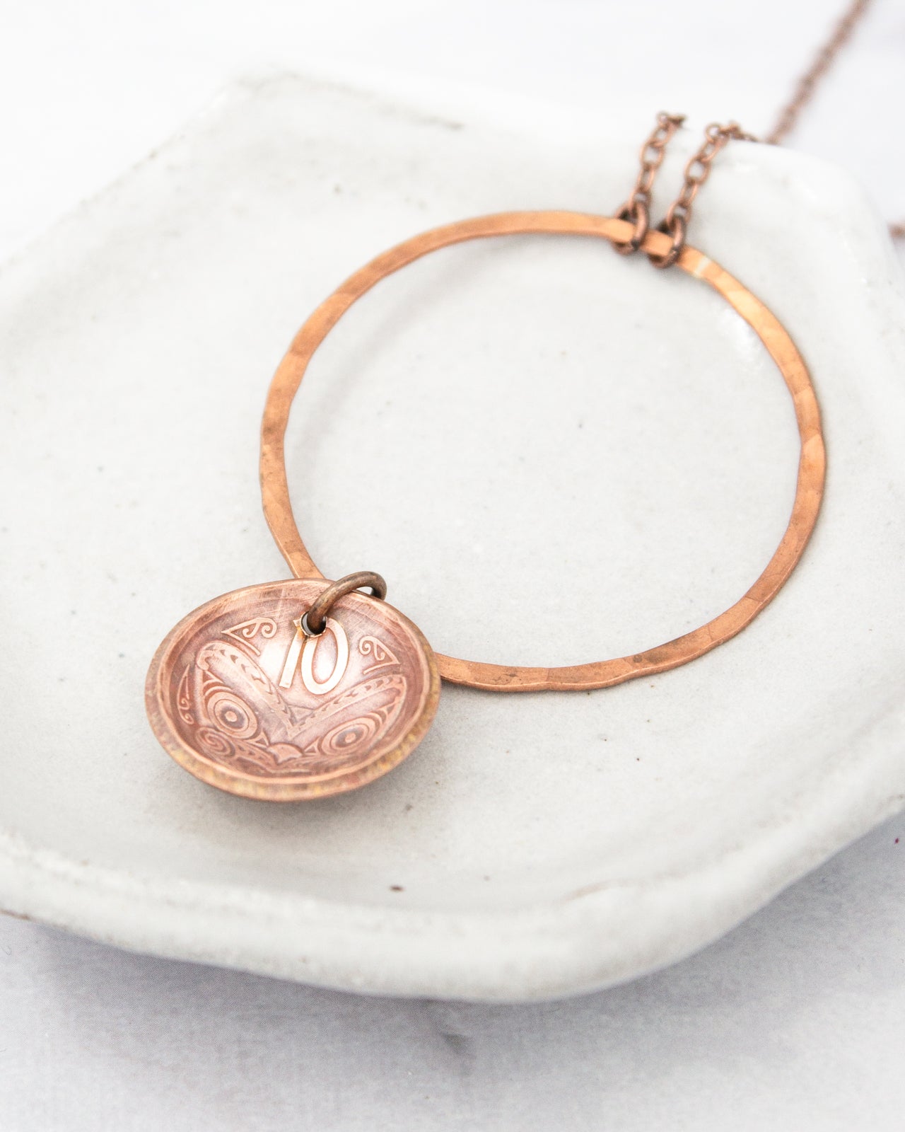A necklace with a pendant featuring a design resembling a 10-cent coin.