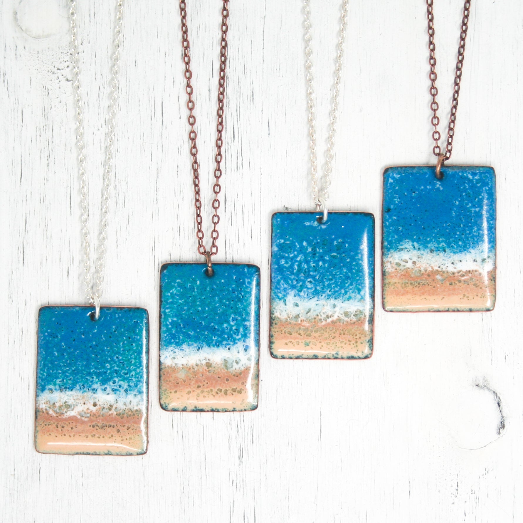 three square necklaces with a beach scene on them