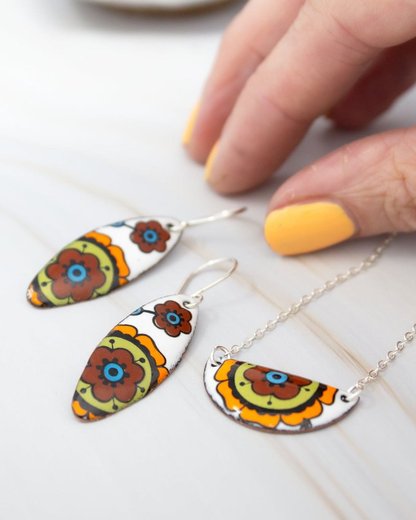 A hand is holding a pair of colorful earrings and a necklace with a floral design.