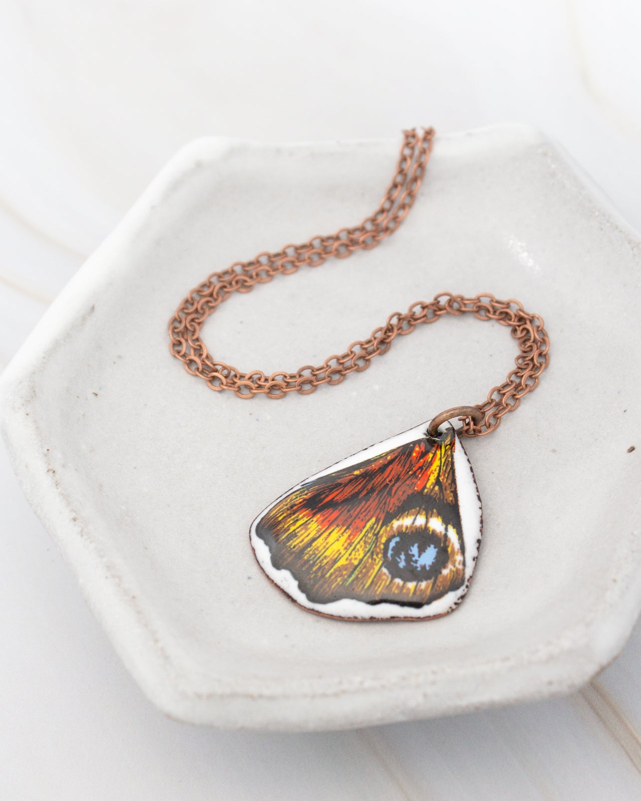 A necklace with a pendant featuring a colorful butterfly wing design rests on a white plate.