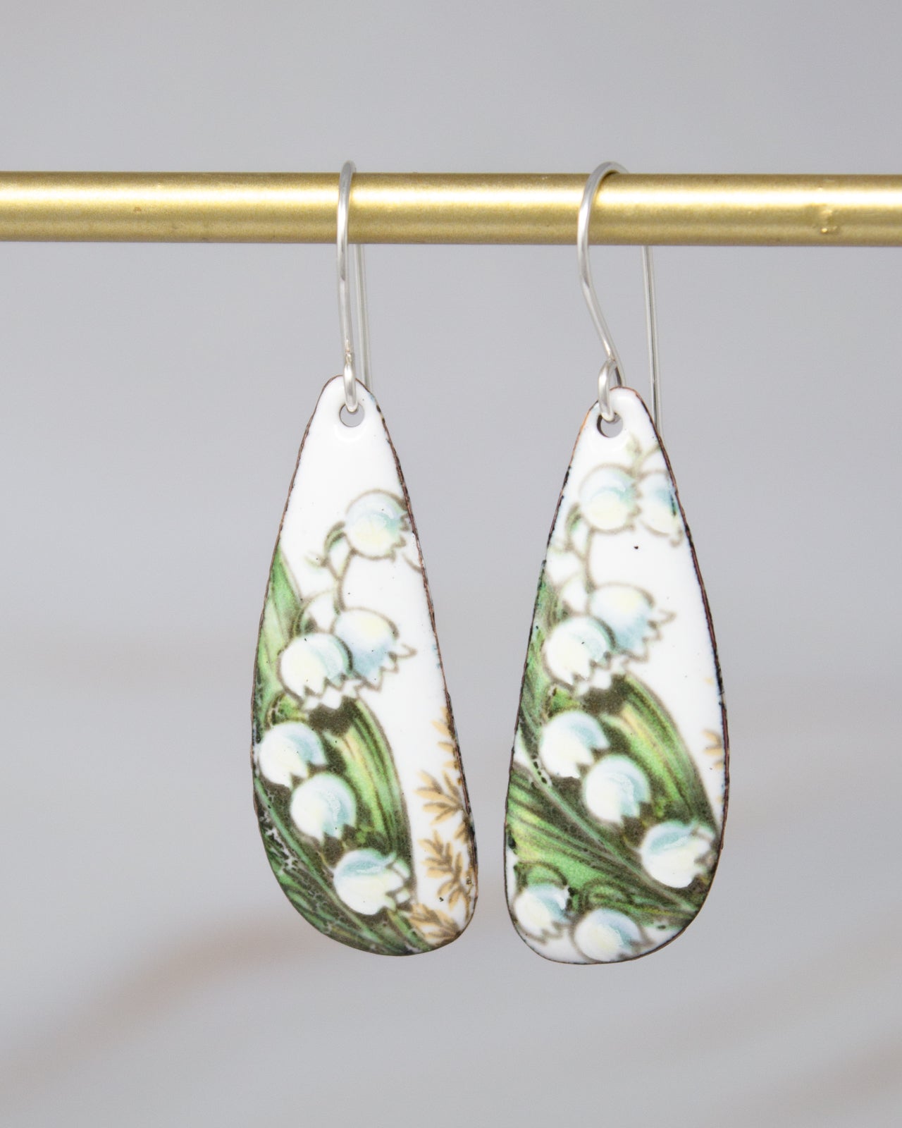 A pair of earrings with a floral design, featuring white flowers and green leaves.