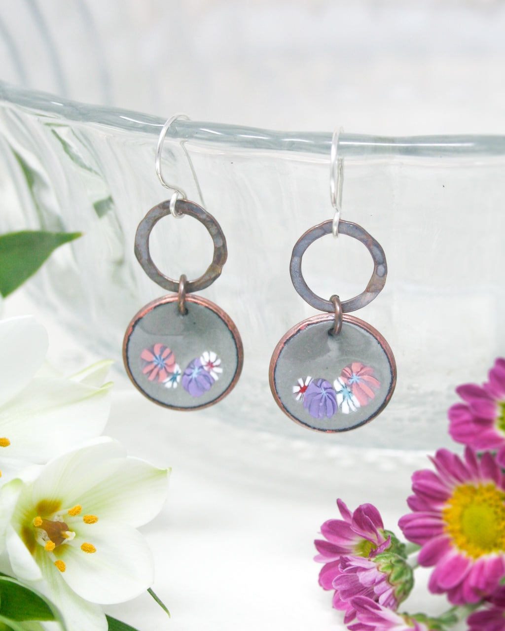 a close up of a pair of earrings with flowers in the background