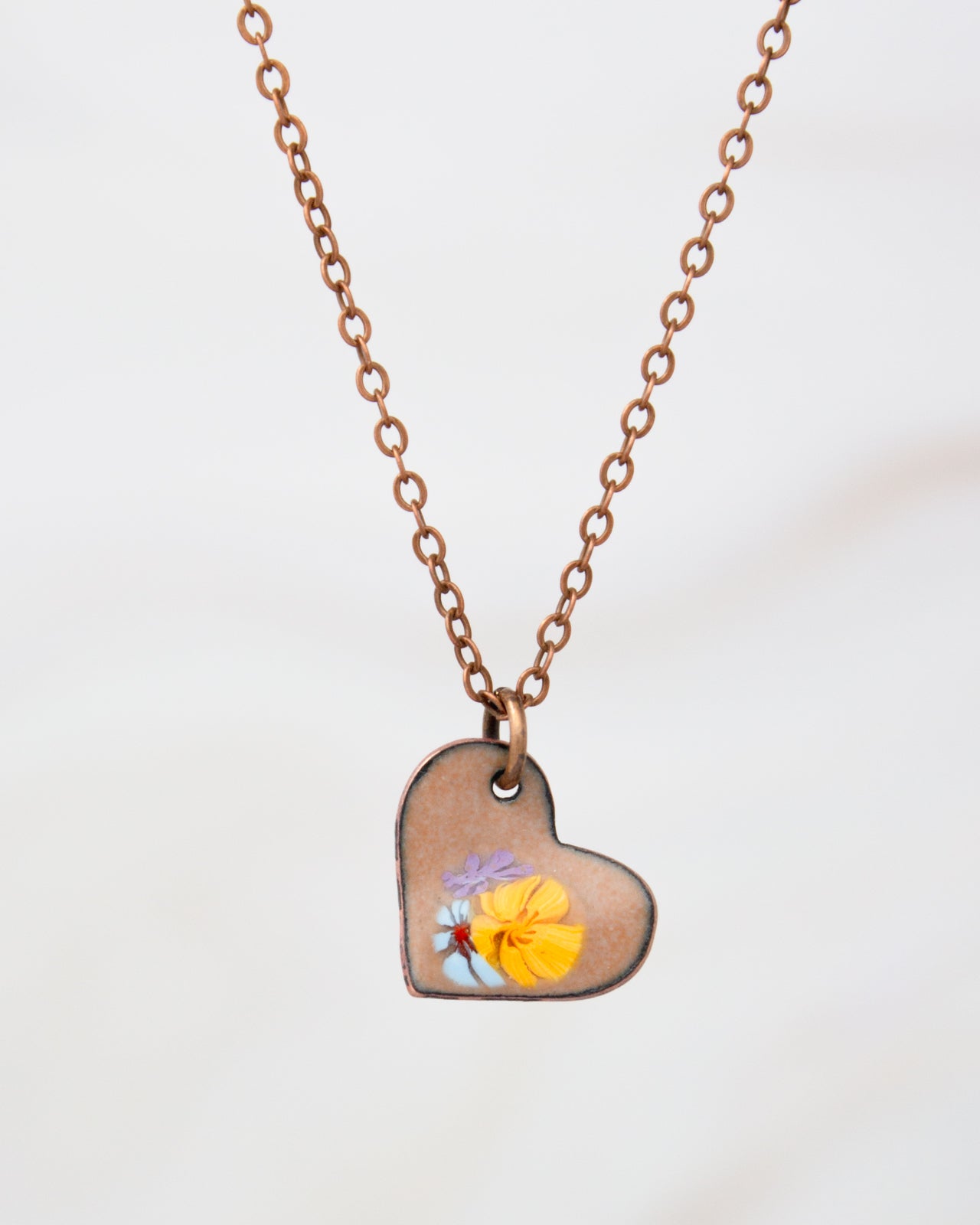 A heart-shaped pendant necklace with a small flower design on it.