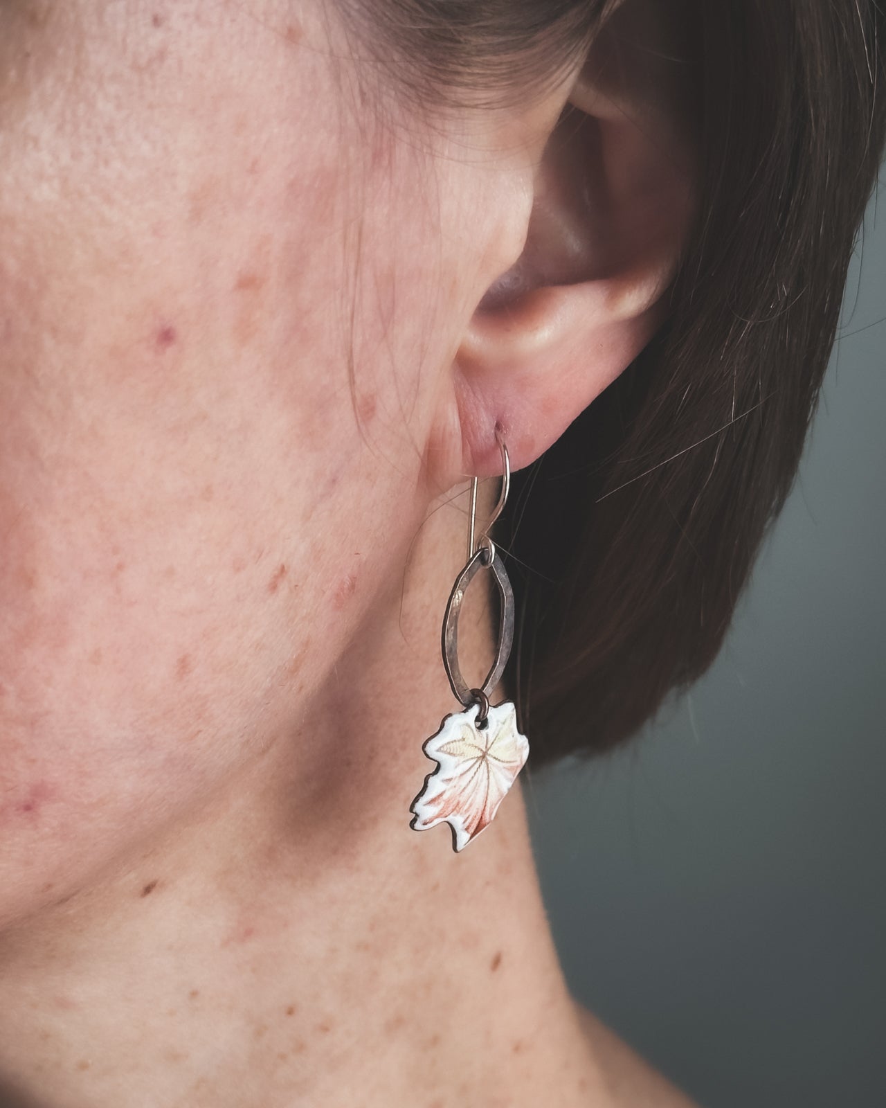 A close-up view of a person's ear, showing a pair of silver earrings with a leaf design hanging from the earlobe.