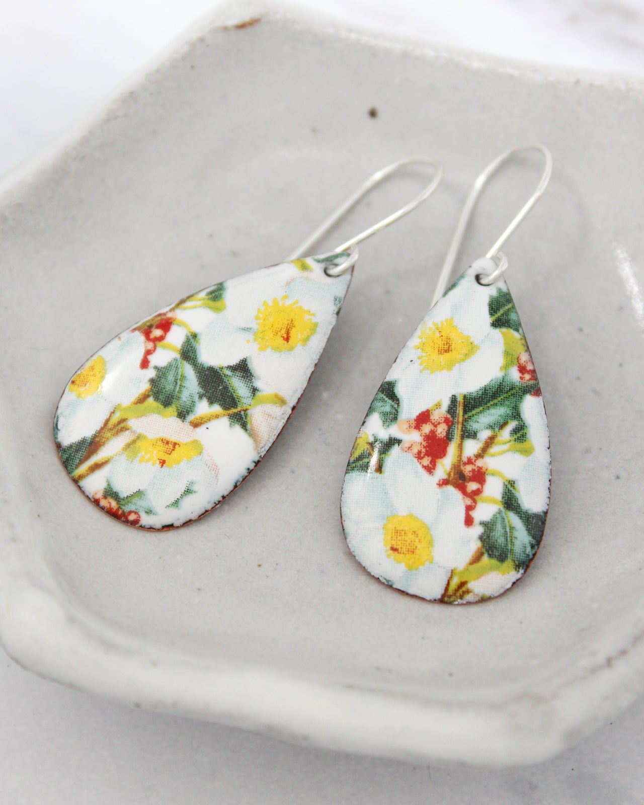 A pair of earrings with a floral pattern on the pendants, resting on a white surface.