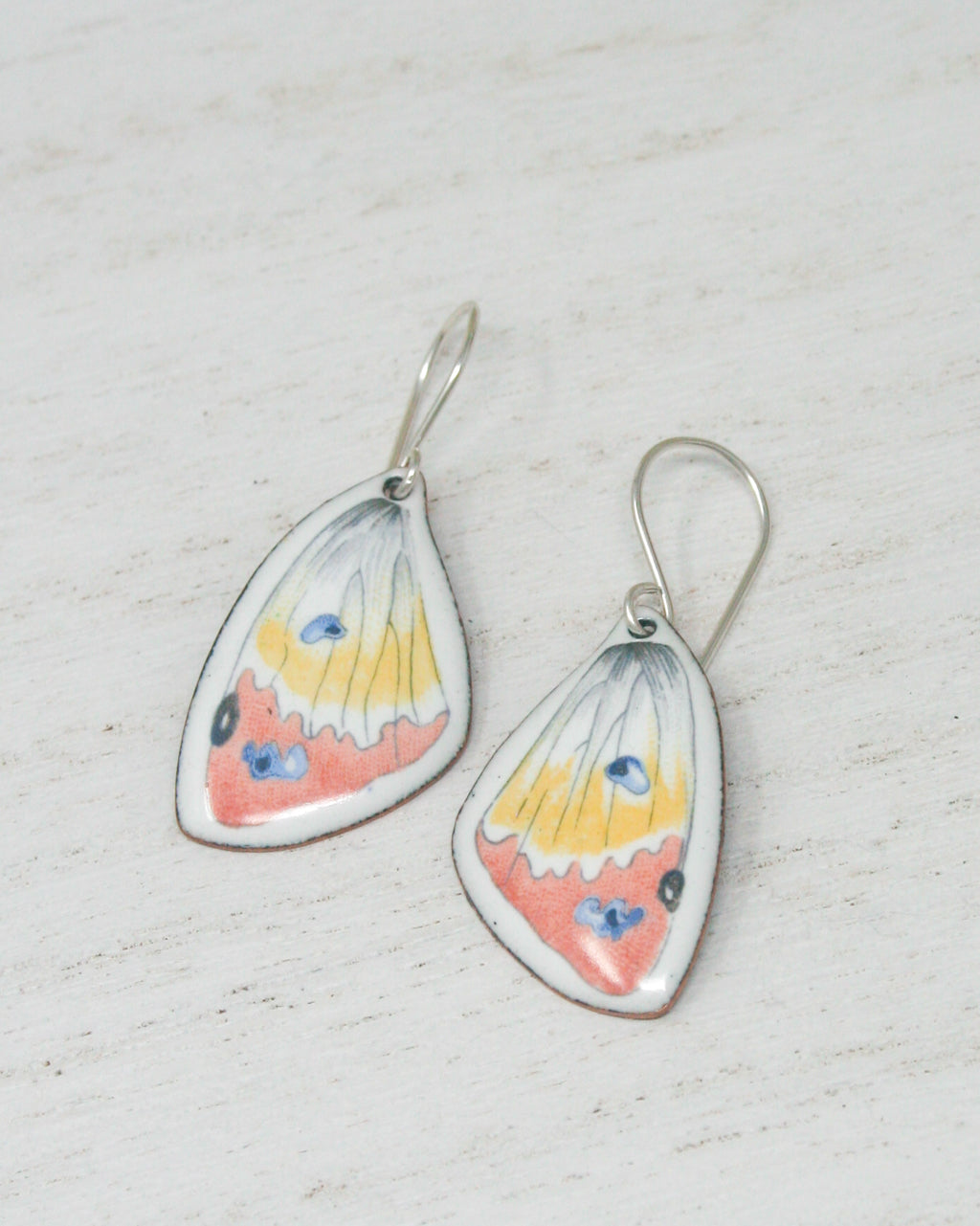 a pair of earrings with butterfly wing designs, resting on a white surface.