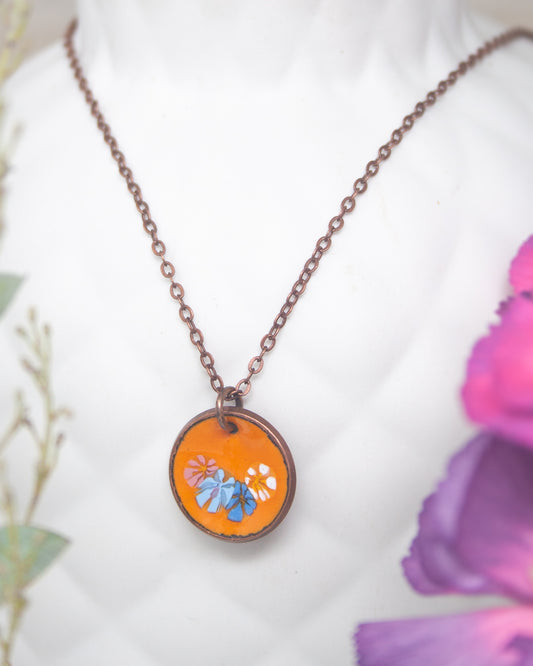 A necklace with a circular pendant featuring a floral design in orange and blue colors.