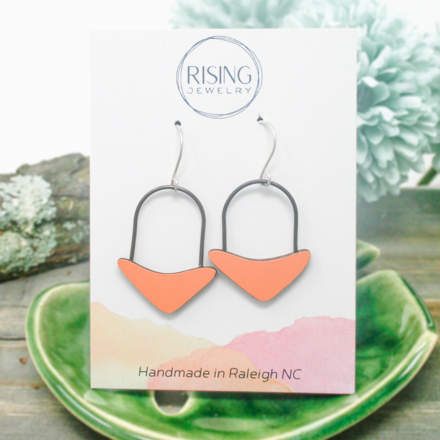 a pair of orange and silver earrings sitting on top of a green plate