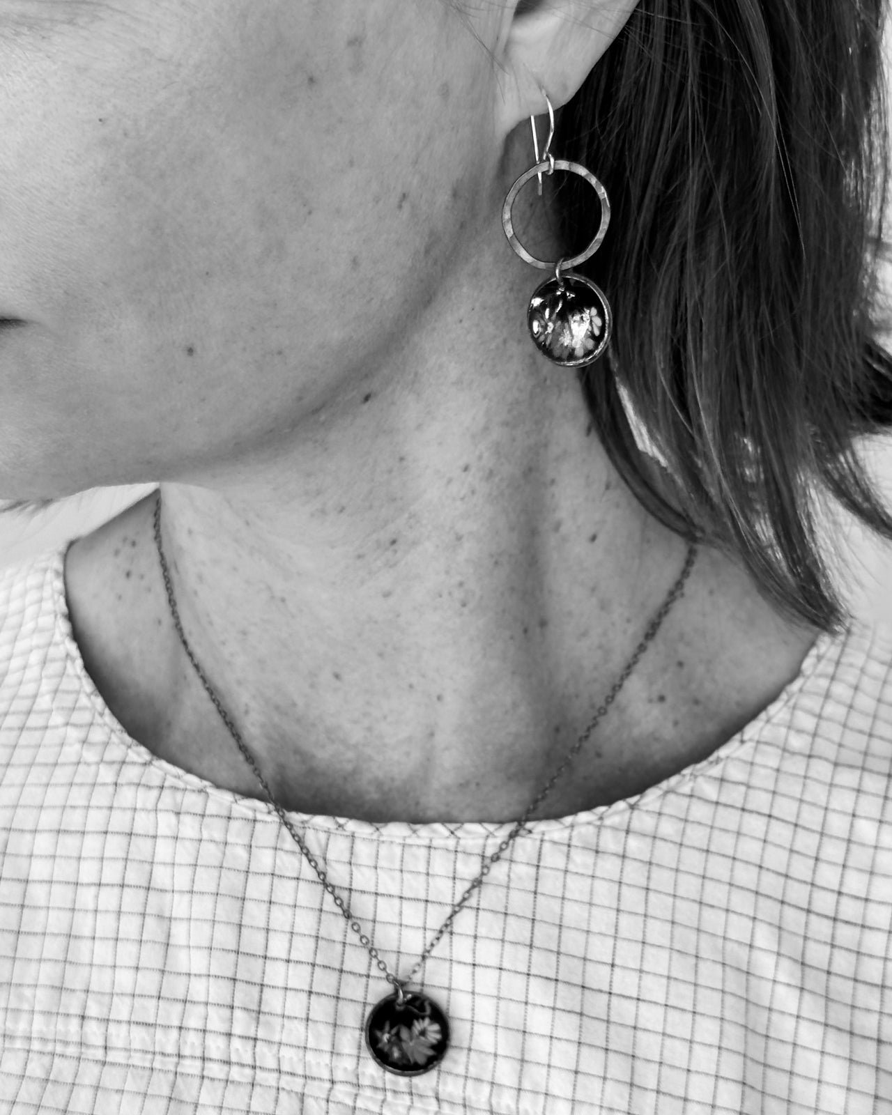 A close-up of a person's neck and ear, featuring a necklace with a pendant and a pair of dangling earrings.