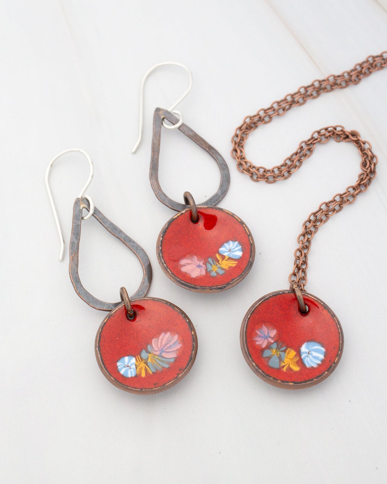 a pair of red earrings and a necklace with a floral design.