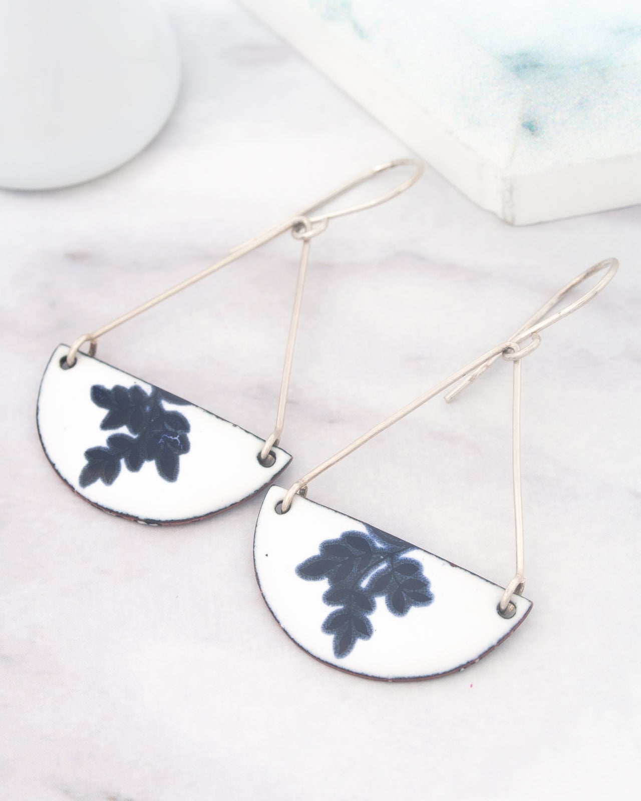 A pair of white earrings with blue leaf designs on them, hanging from a wire.