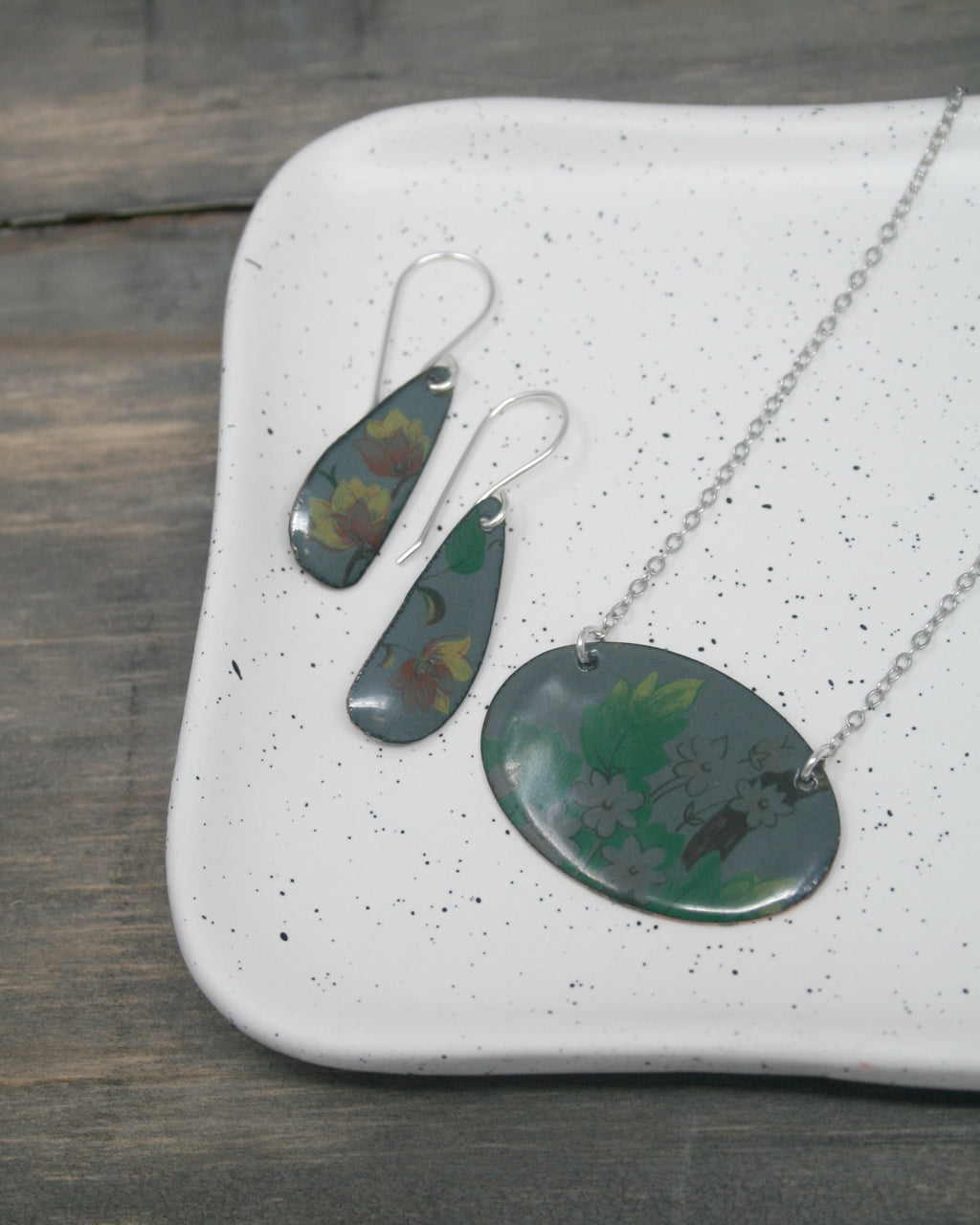 a pair of earrings and a necklace displayed on a white speckled plate.