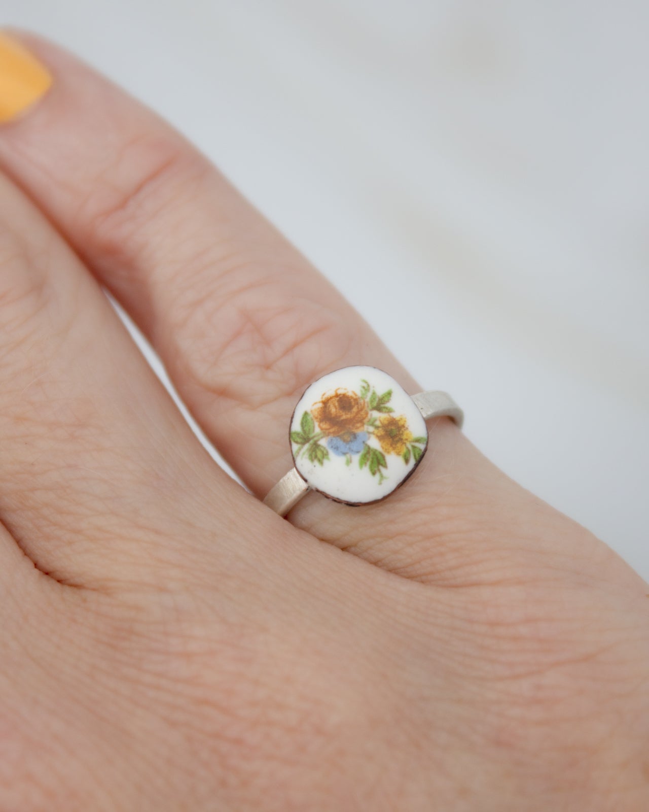 A close-up of a person's hand wearing a ring with a floral design on it.