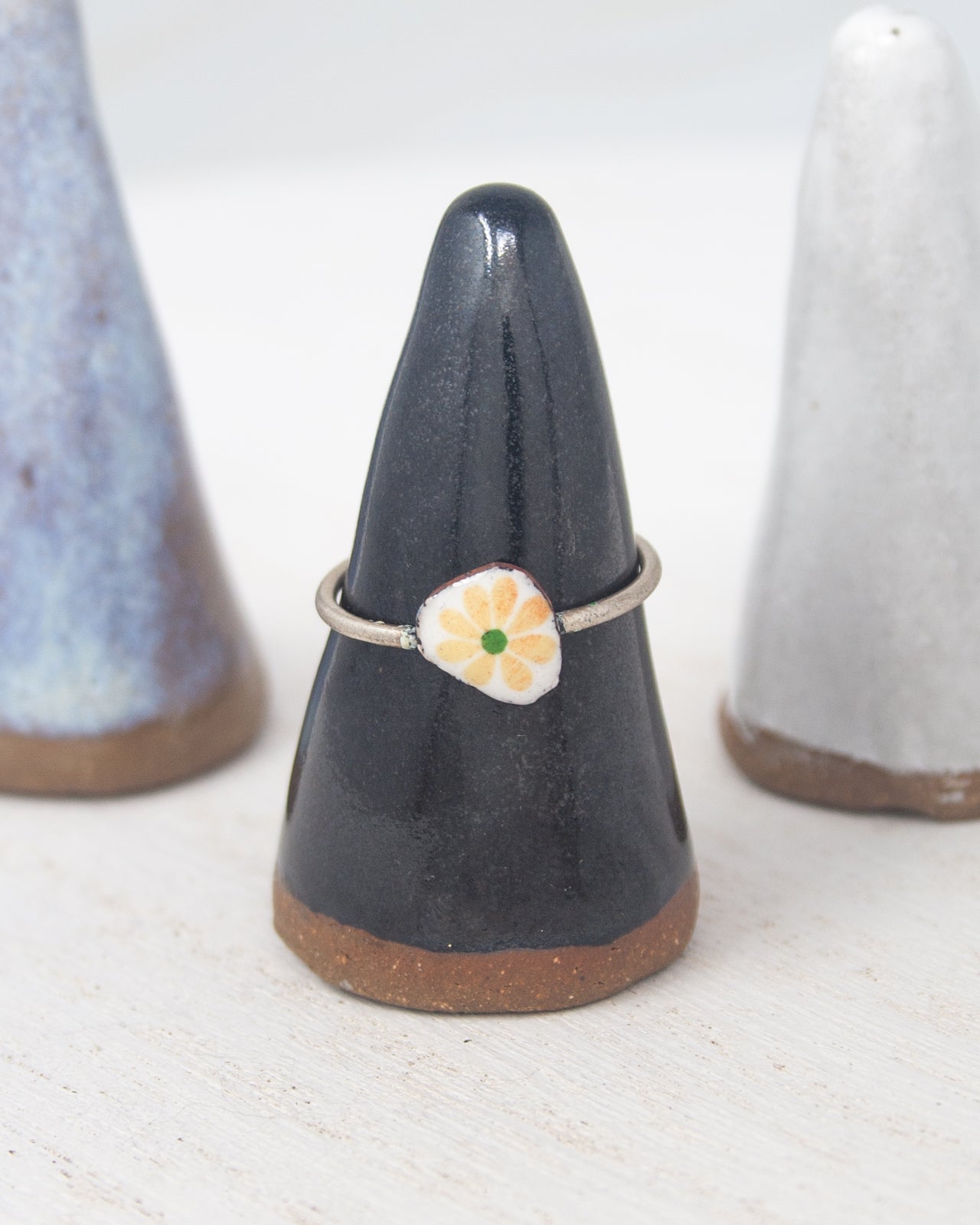 A black ceramic ring stand with a white and yellow flower design on it, placed between two white ceramic objects.