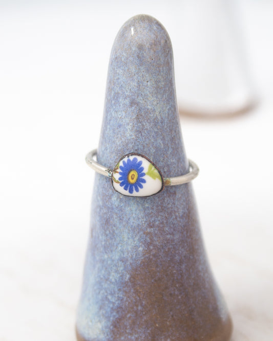 A ring with a blue flower design on it, displayed on a ceramic stand.