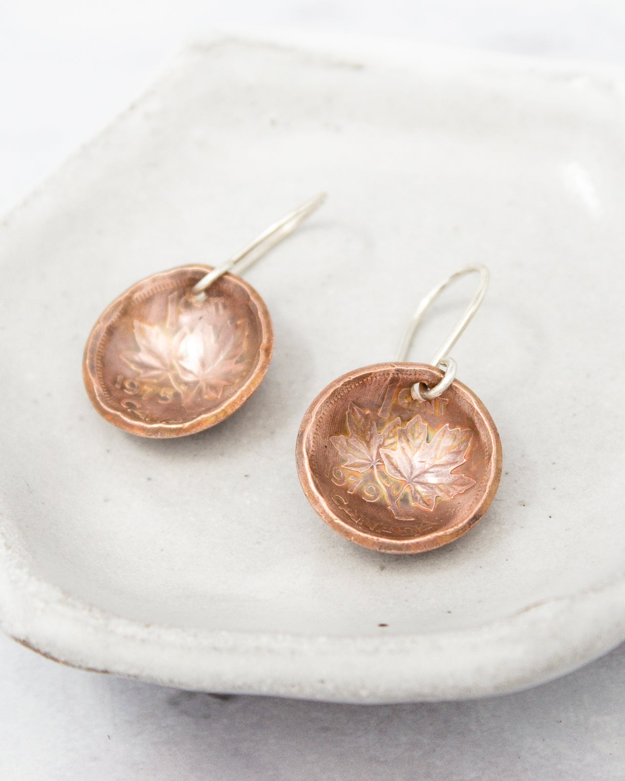 a pair of copper-colored earrings with leaf designs, displayed on a white plate.