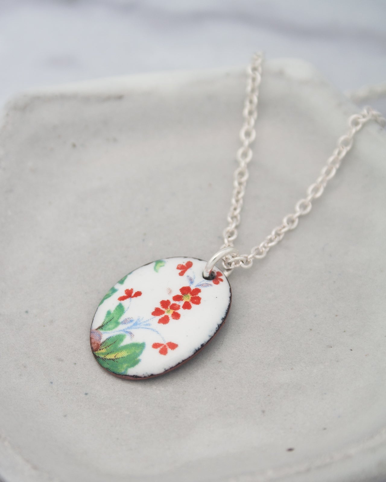 A necklace with a pendant featuring a floral design in red, green, and yellow colors.
