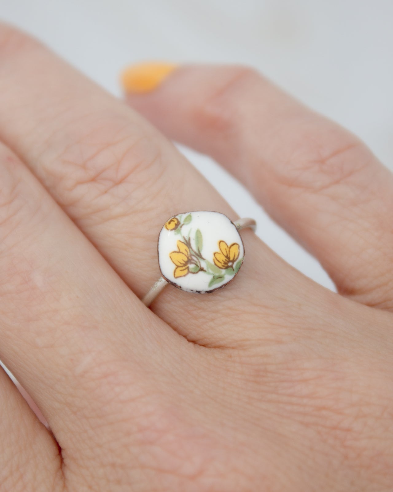 A close-up of a person's hand wearing a ring with a floral design on the finger.