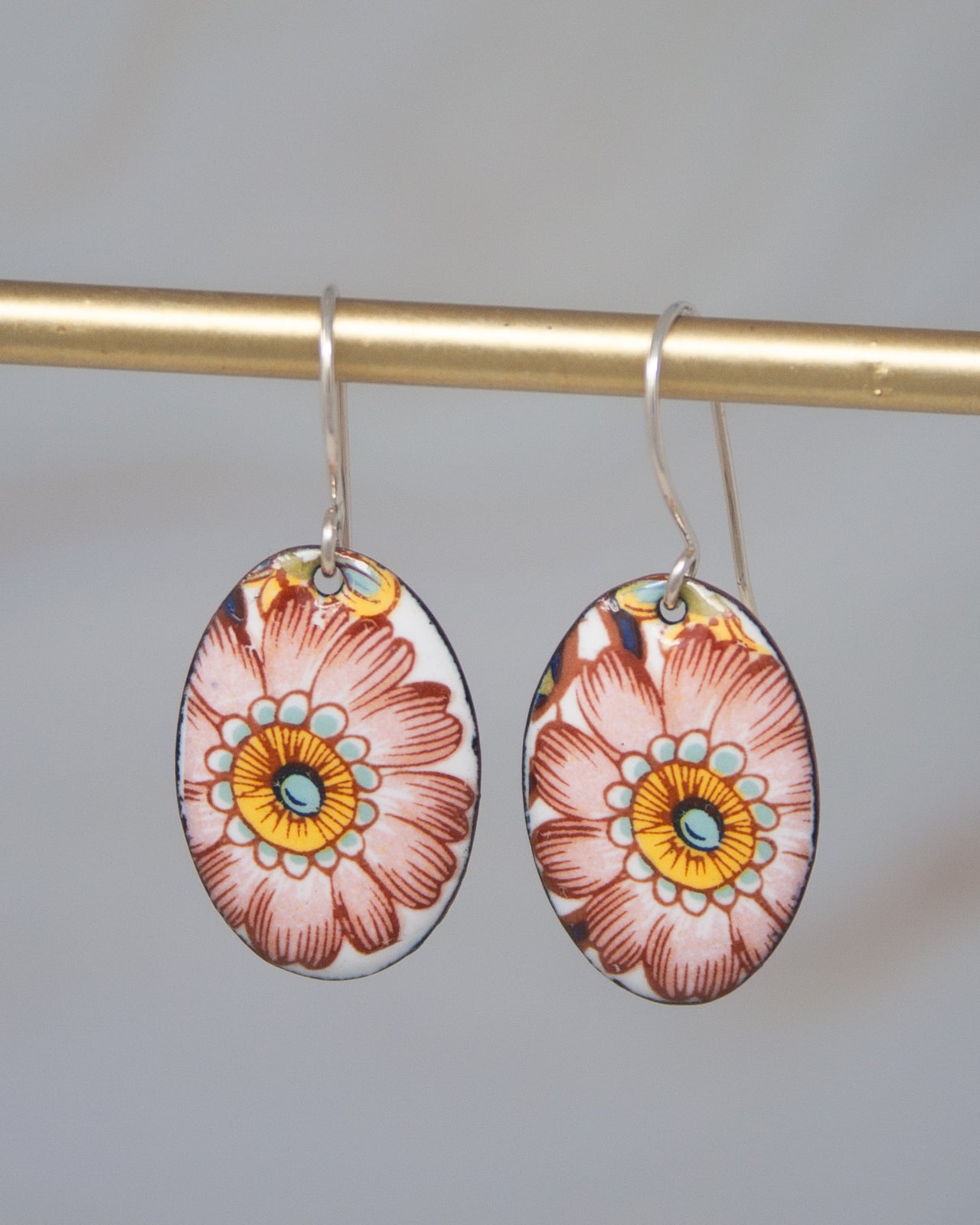 A pair of earrings with a floral design, hanging from a gold-colored metal hook.
