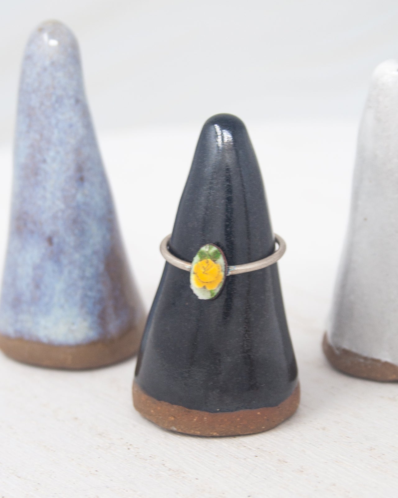 A black ceramic ring stand with a yellow flower on it, placed between two white ceramic stands.