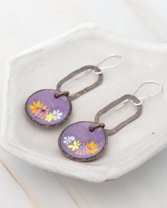 A pair of purple earrings with a floral design, displayed on a white plate.