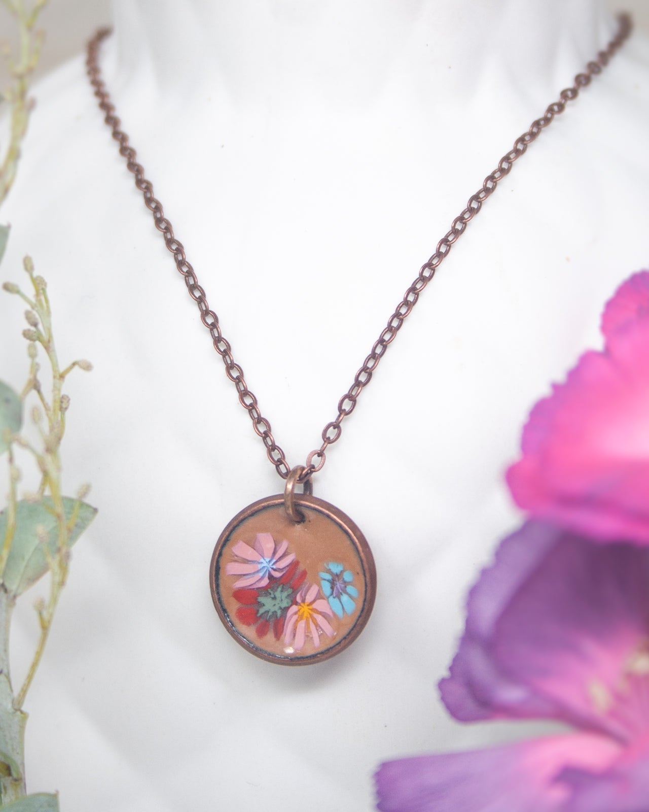 A necklace with a circular pendant featuring a floral design, including pink, blue, and green flowers.