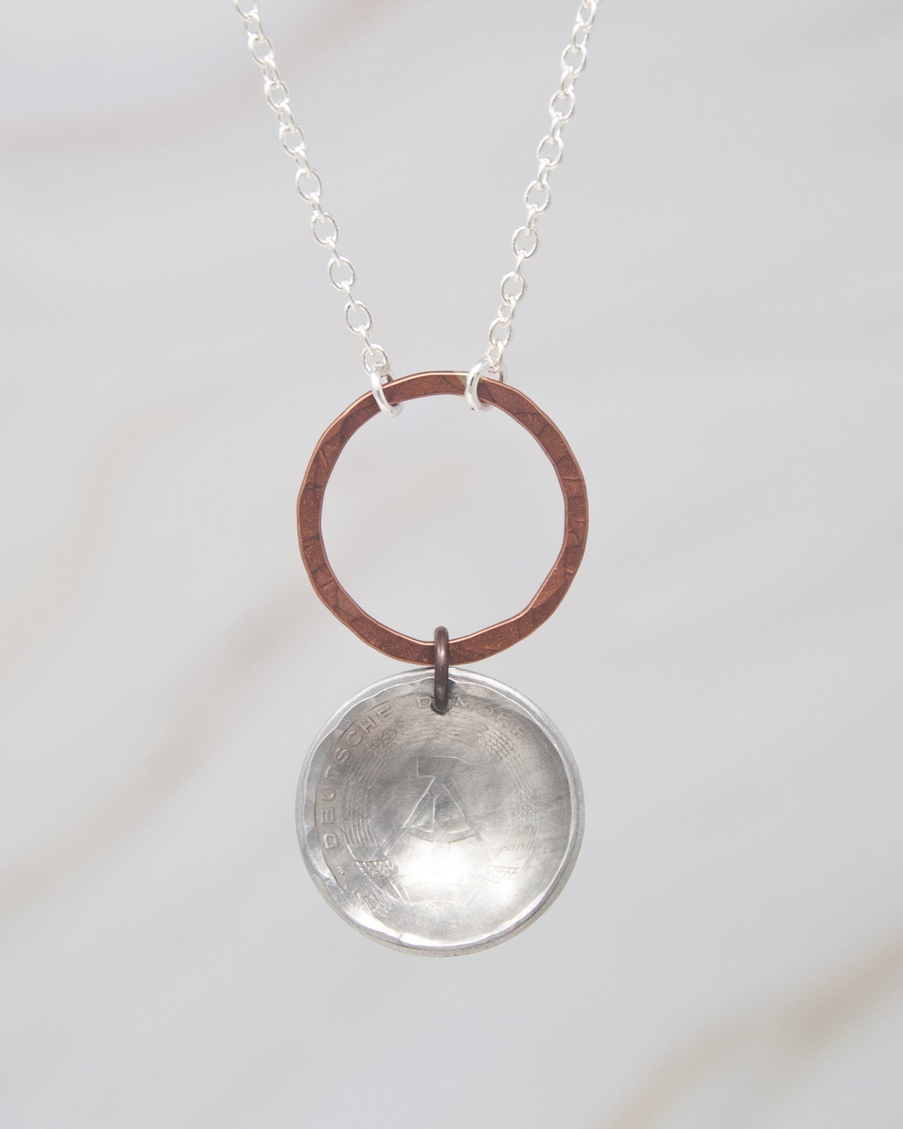 A silver necklace with a circular pendant featuring a metallic design.