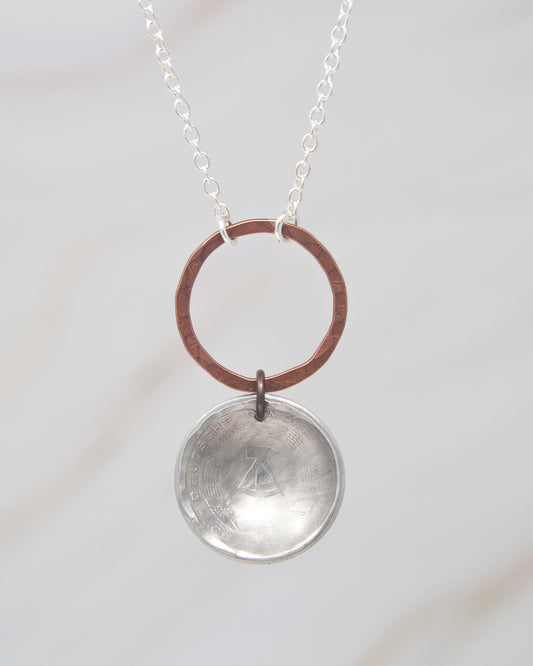 A silver necklace with a circular pendant featuring a metallic design.