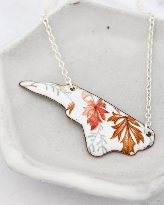 A necklace with a pendant in the shape of a leaf, featuring a floral design with red and orange leaves.