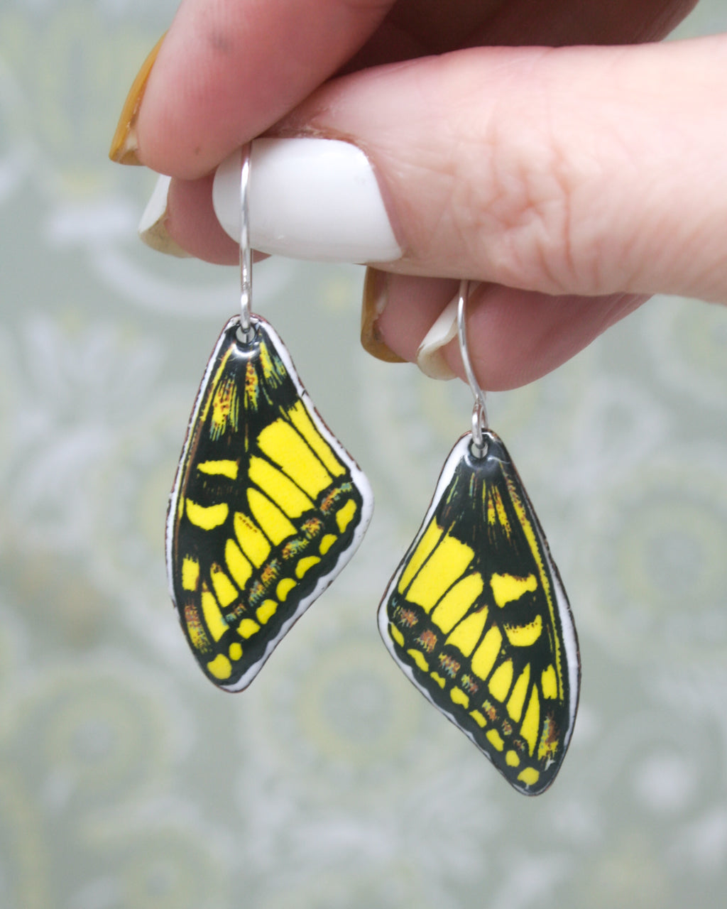 a hand holding a pair of yellow and black butterfly earrings