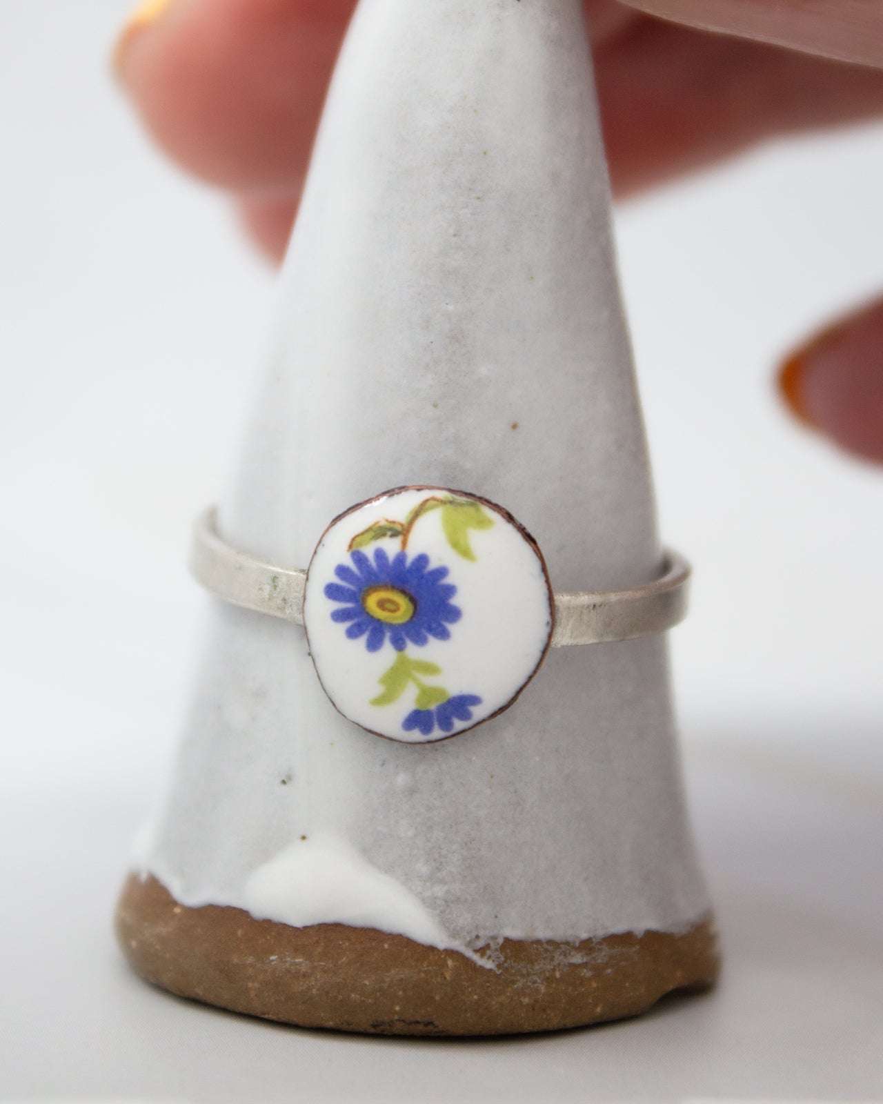 A hand is holding a white ceramic ring with a blue and green floral design on it.
