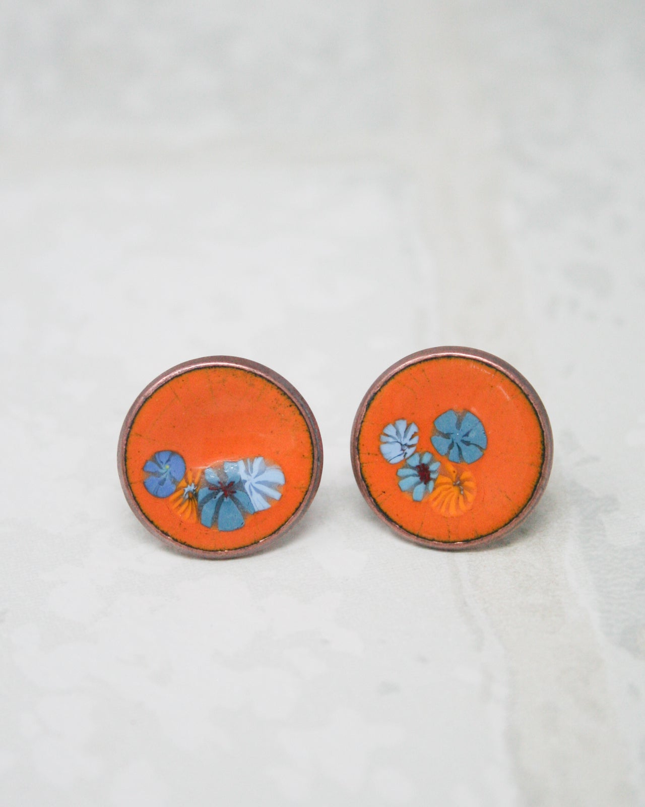 two round, orange-colored earrings with blue floral designs on them.
