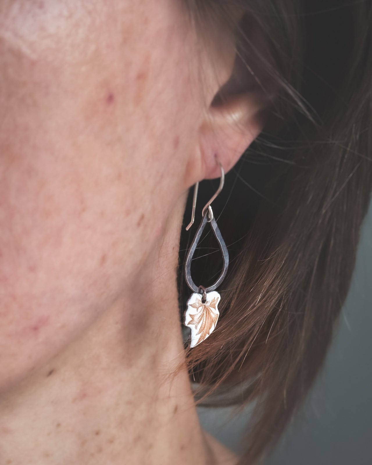 A close-up view of a person's ear with a leaf-shaped earring hanging from the earlobe.