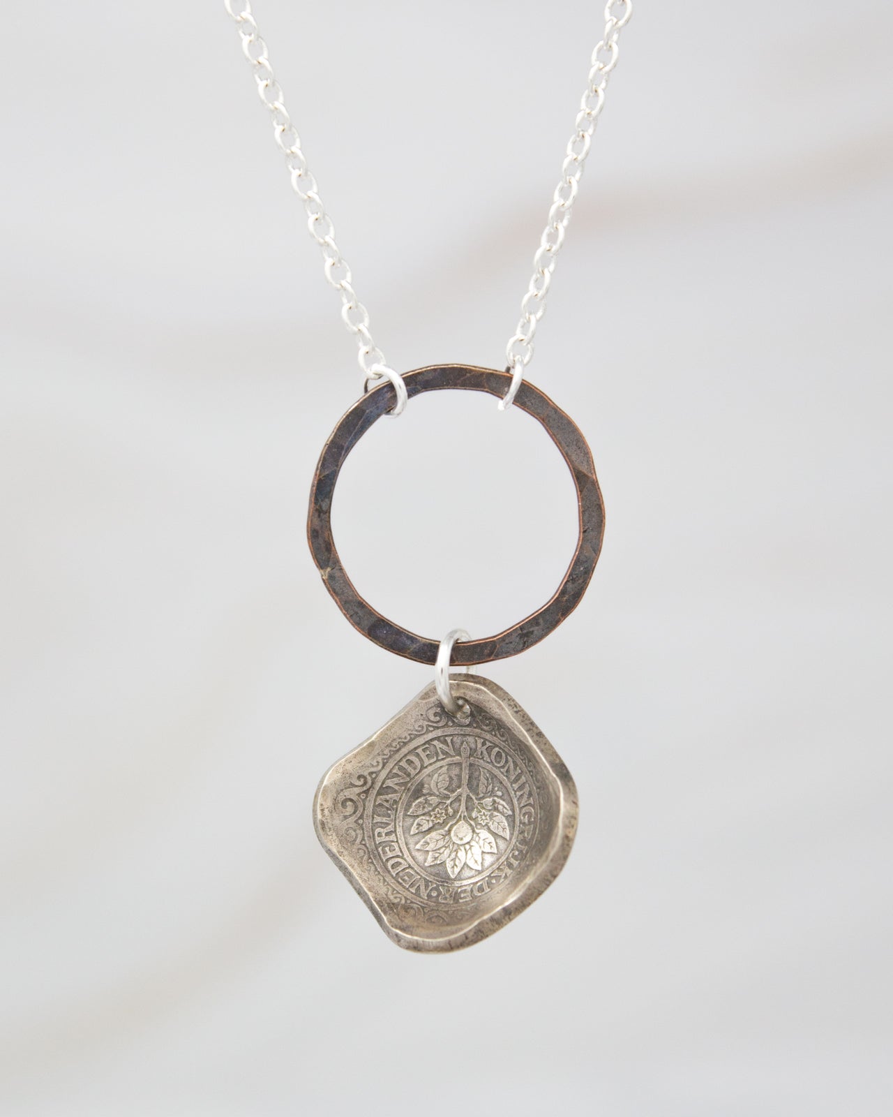 A silver necklace with a pendant featuring a circular design and a textured element.