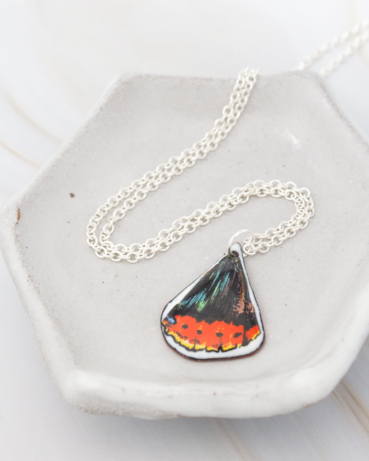 A necklace with a pendant featuring a colorful butterfly design rests on a white plate.