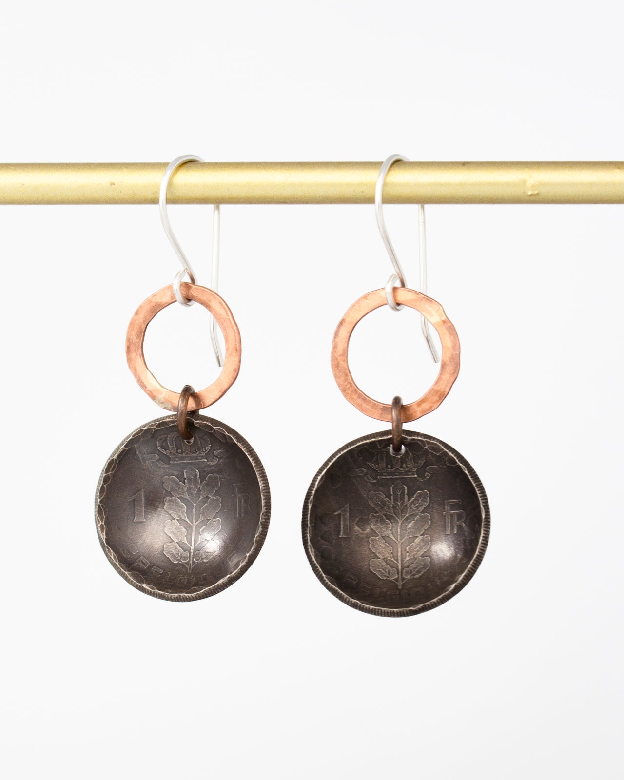 A pair of earrings with a circular design and a metallic ring, hanging from a gold-colored hook.