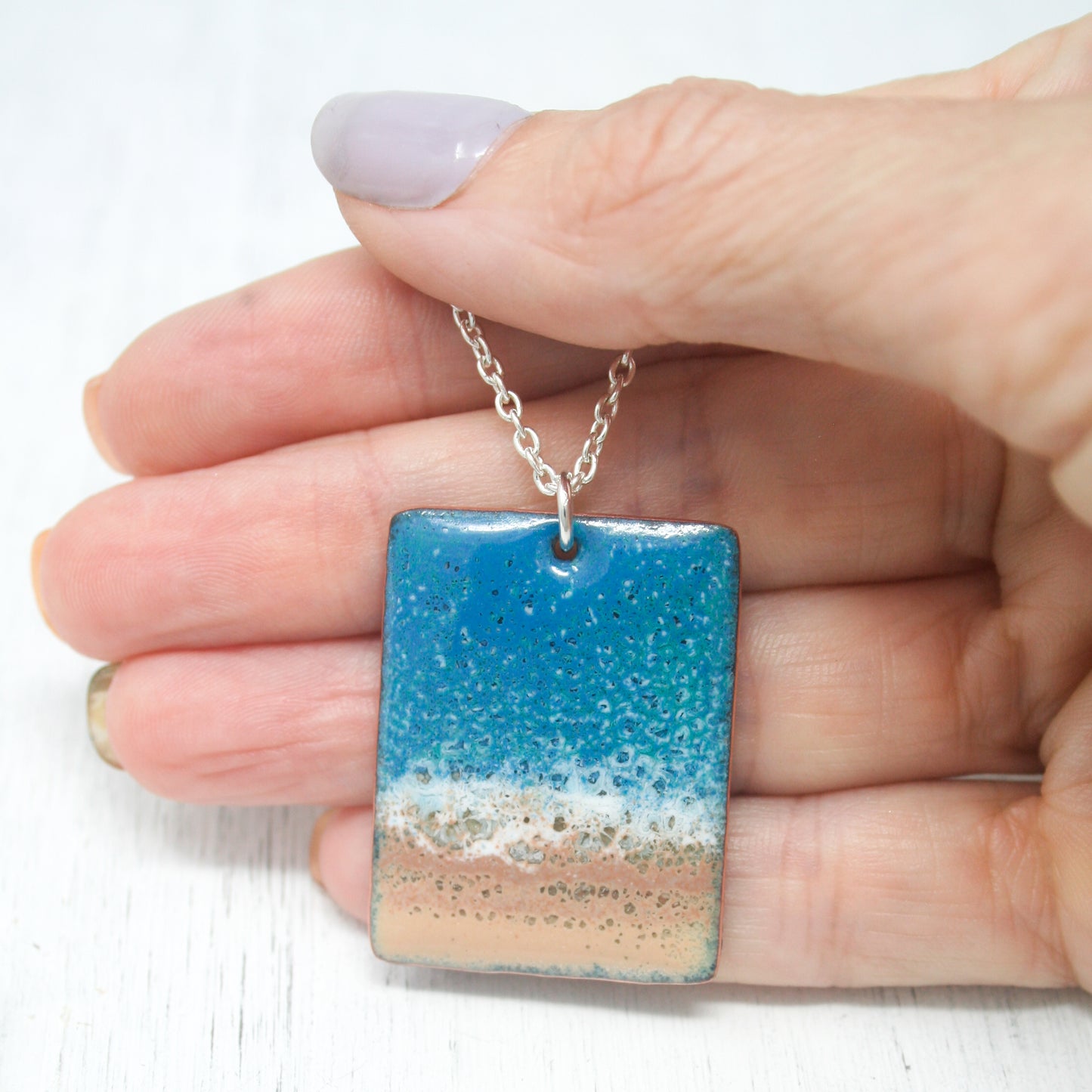 a hand holding a blue and white square pendant