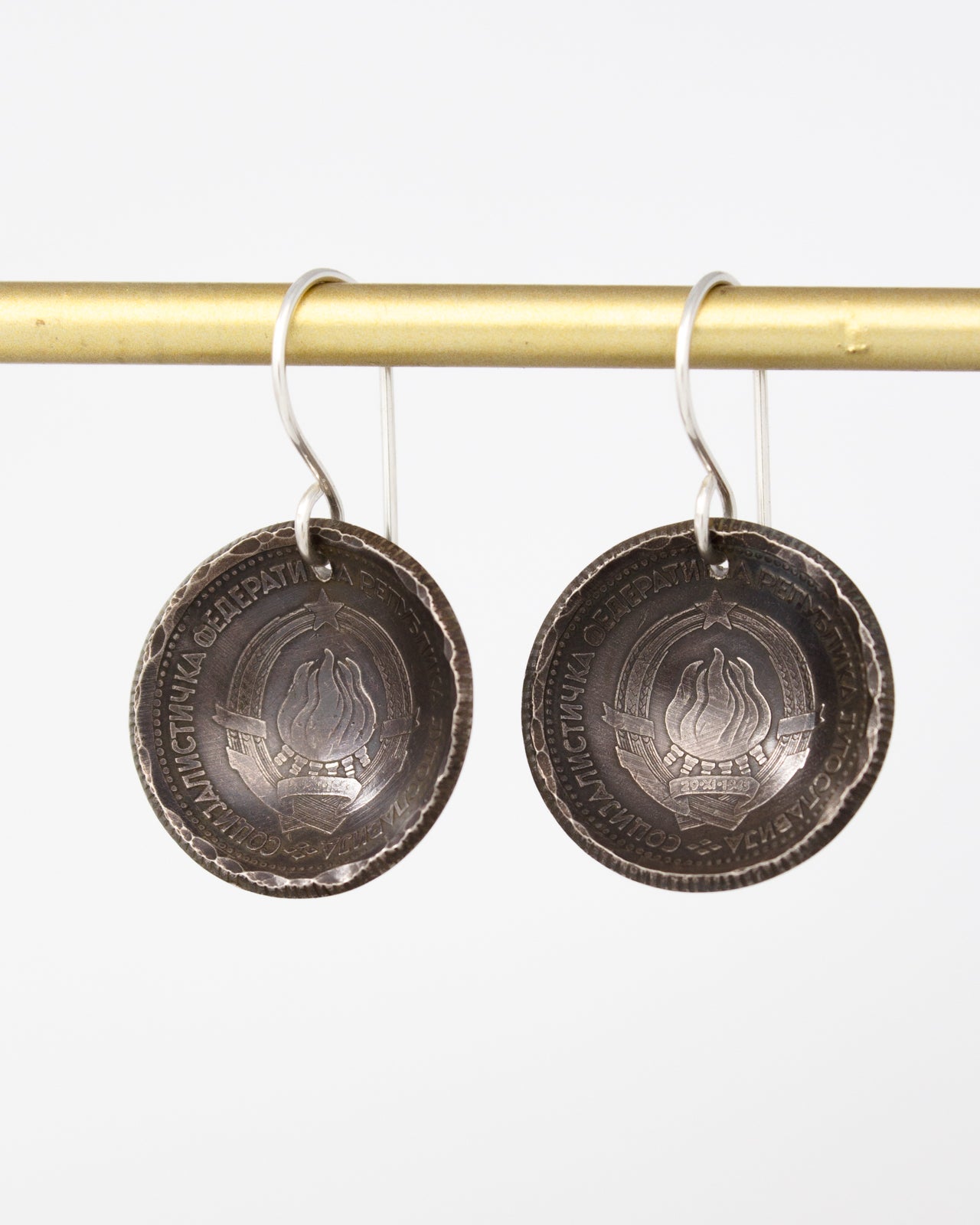 A pair of silver earrings with a circular design hanging from a gold bar.