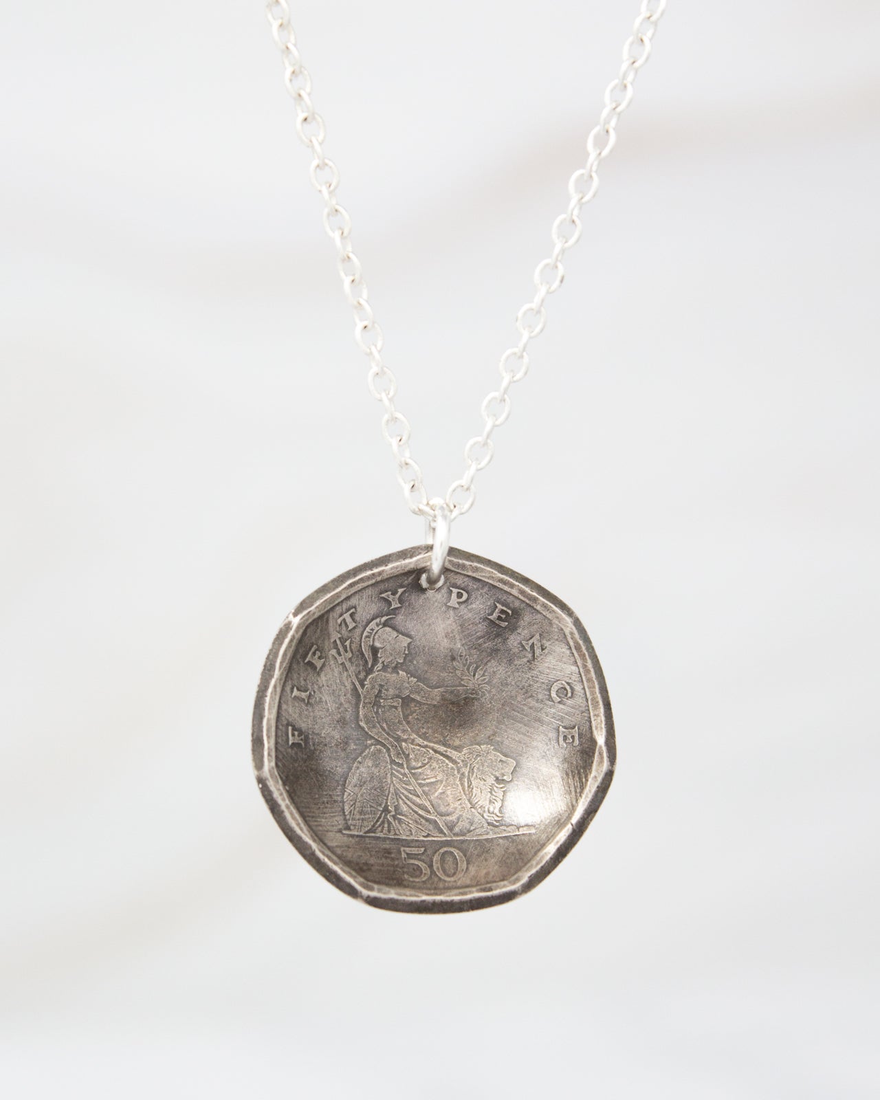 A silver necklace with a pendant in the shape of a British 50 pence coin.