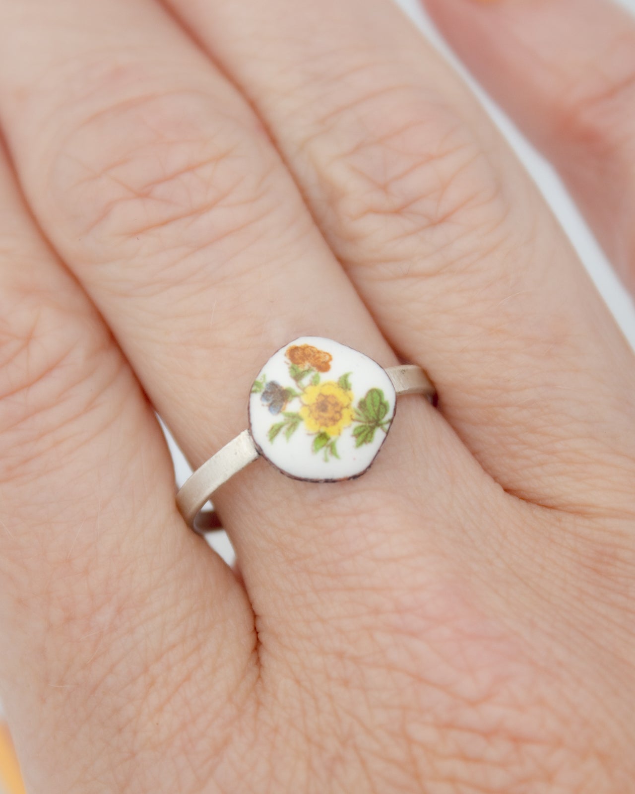 A close-up image of a person's hand wearing a ring with a floral design on the center.