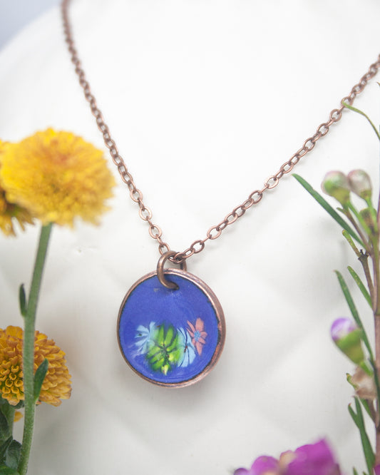 A necklace with a blue pendant featuring a floral design, surrounded by yellow and purple flowers.
