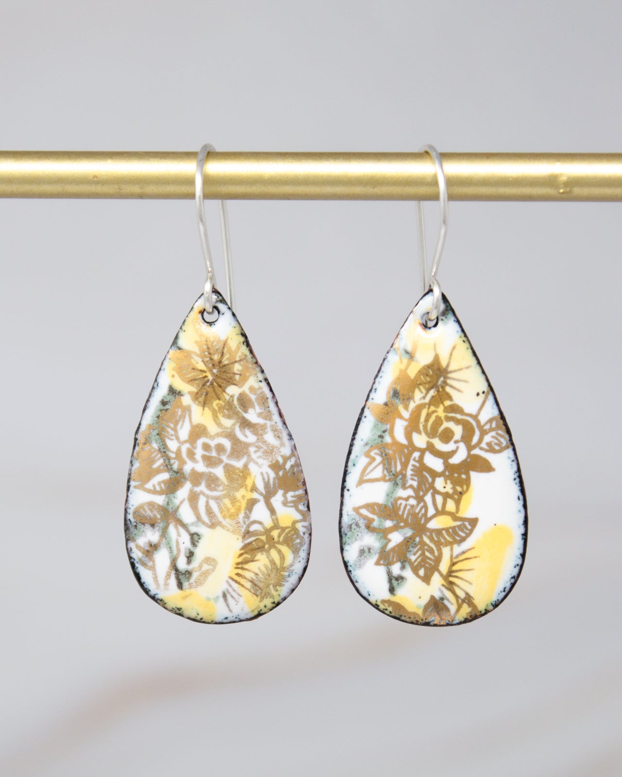 A pair of earrings with a floral design, hanging from a gold-colored metal hook.
