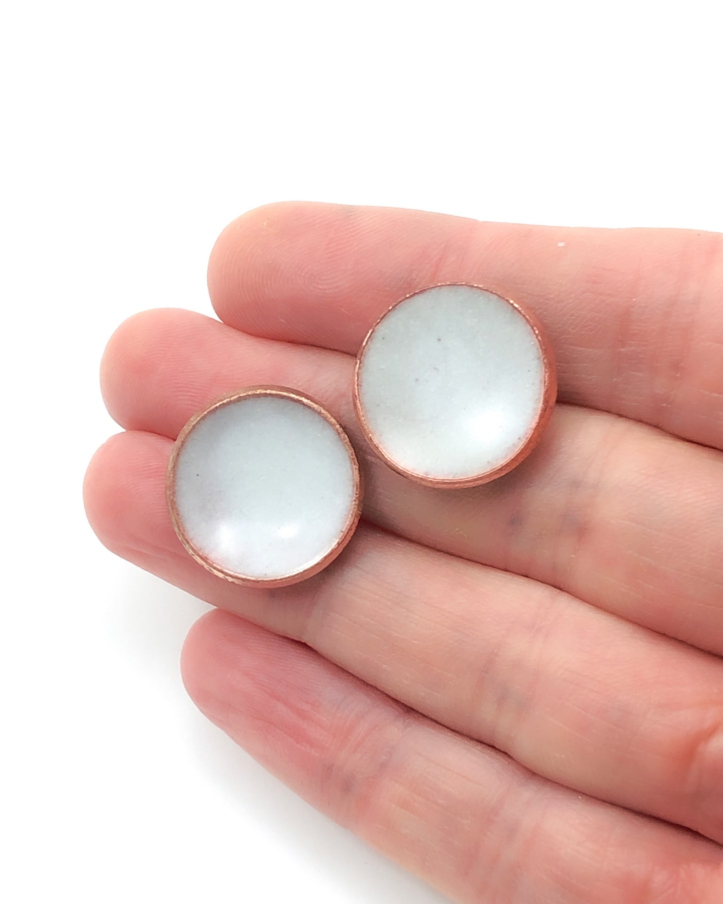 a pair of small white glass cabochons in a hand
