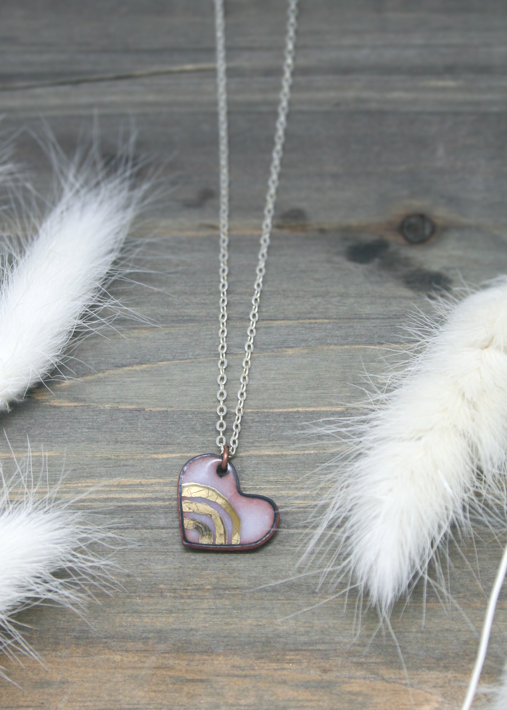 a heart shaped pendant with a feather on a wooden surface