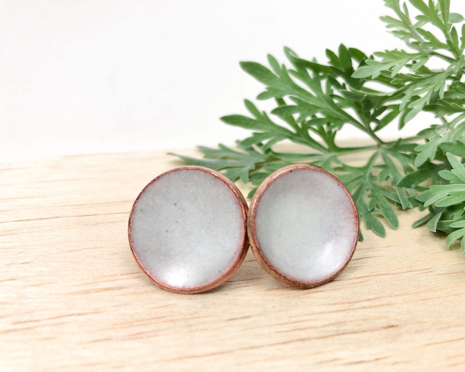a pair of white glass earrings sitting on top of a wooden table