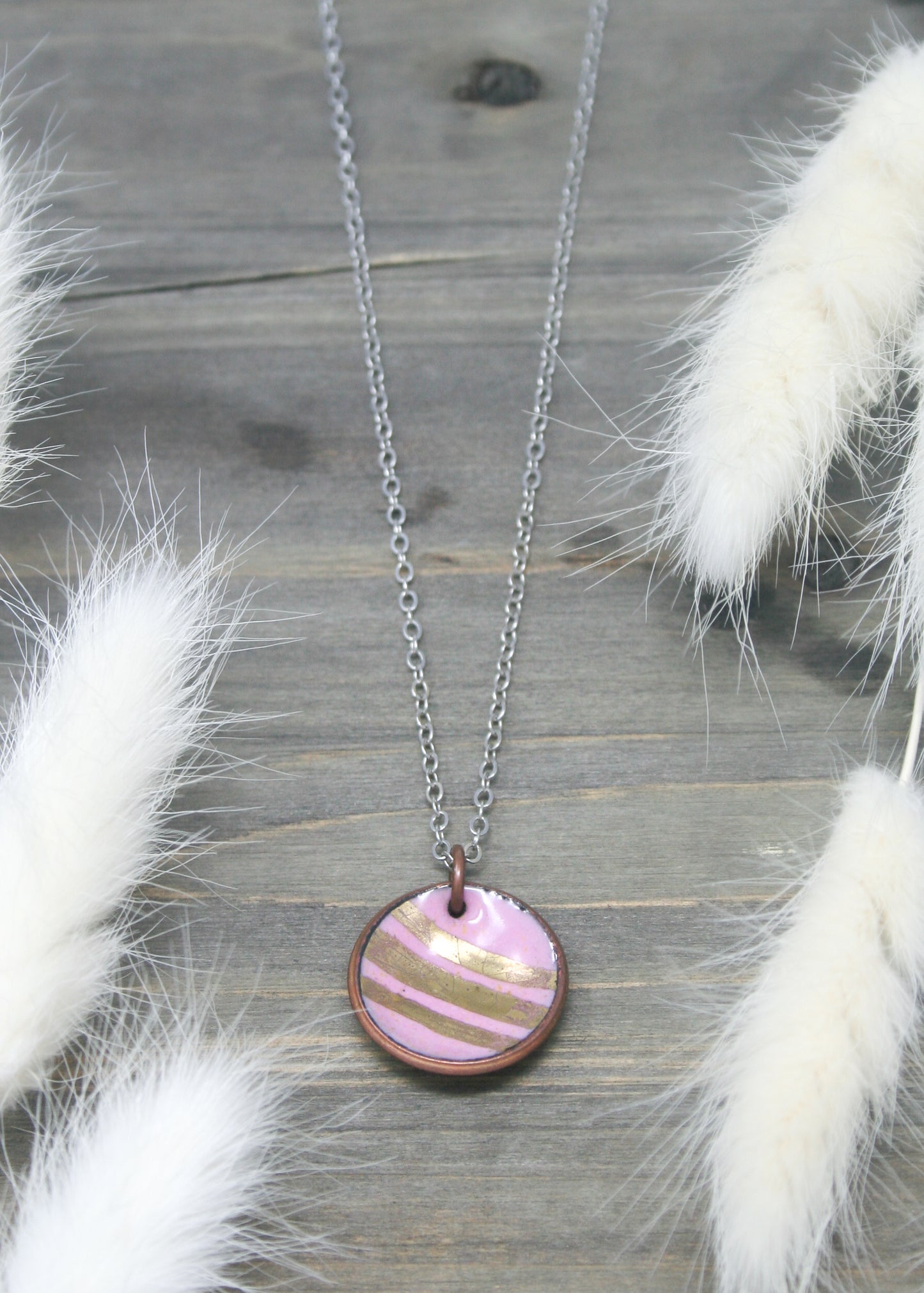 a necklace with a pink and gold striped disc on a chain