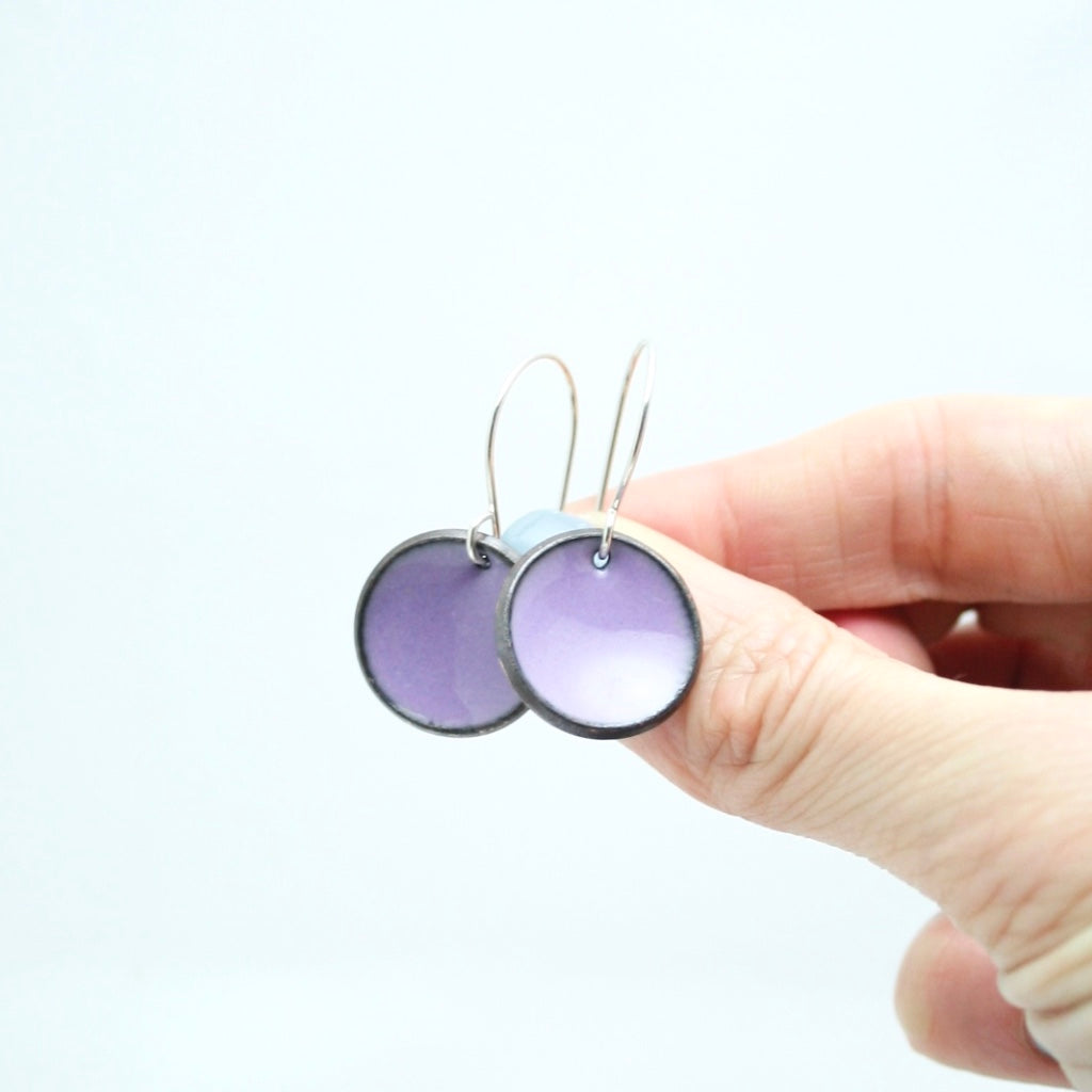 a hand holding two small purple and white earrings