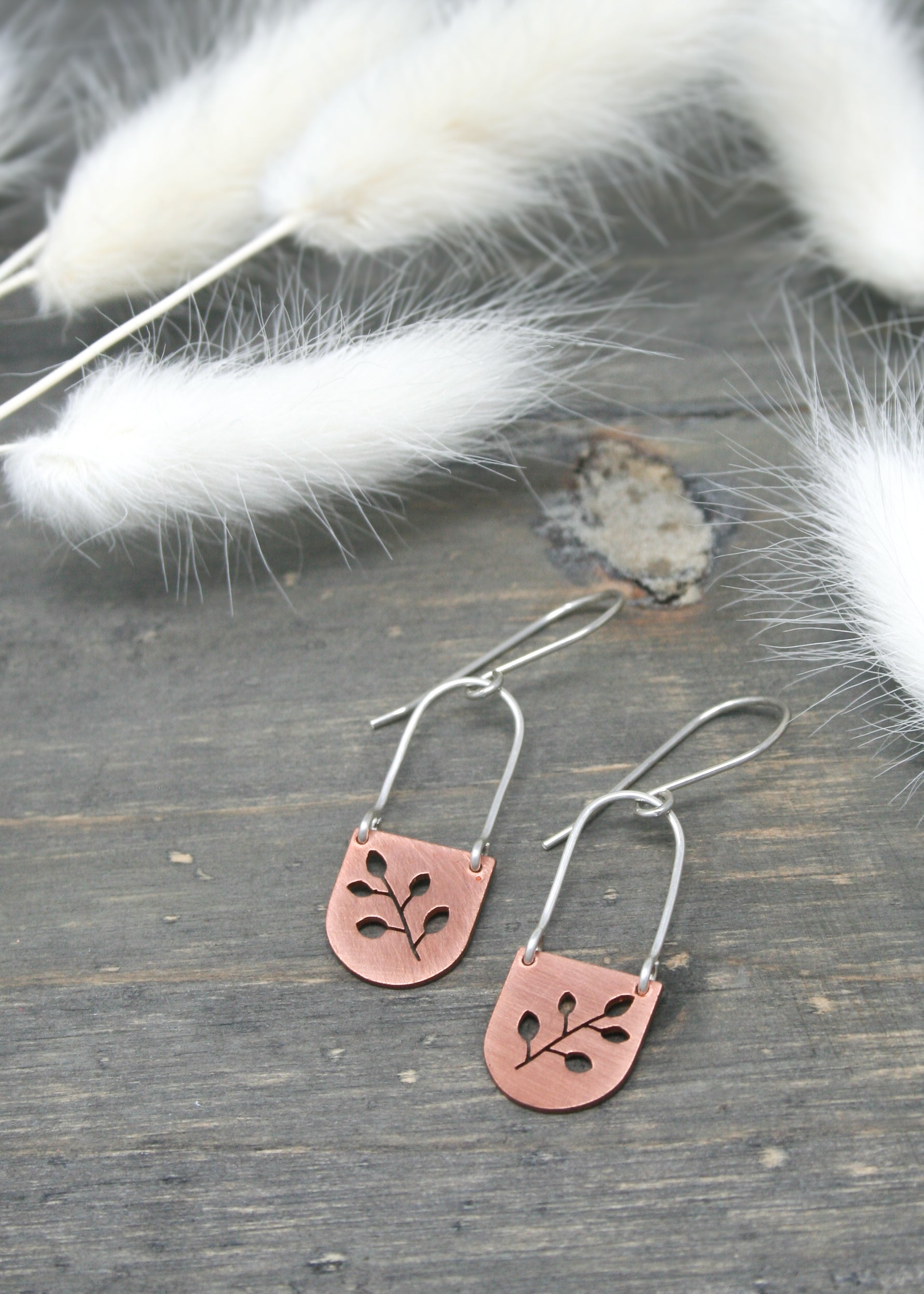a pair of silver and copper earrings on a wooden surface